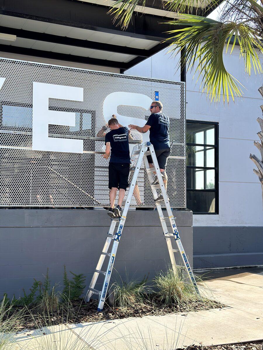 Installation of custom dimensional letters on mesh panels for Dennis+Ives, Jacksonville FL — by CG Signs