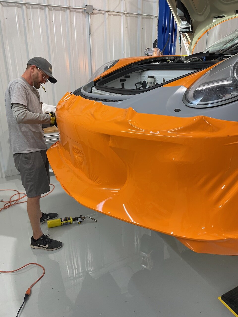 CG Signs technician wrapping a Porsche 911 in matte orange vinyl in the climate-controlled Orange Park shop